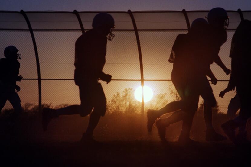 ORG XMIT: S125CDA09 Jogging players kick up dust, as the sun sets behind a giant security...