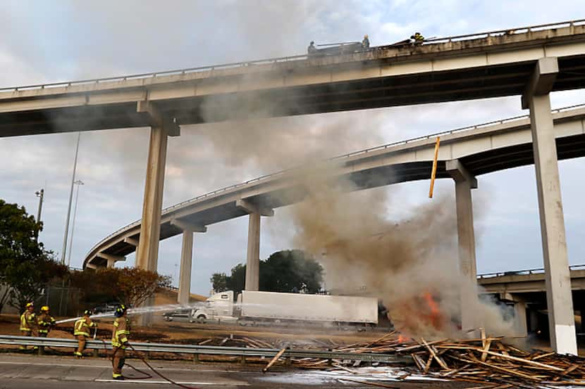  Dallas firefighters douse burning lumber that fell from the scene of a fiery wreck...