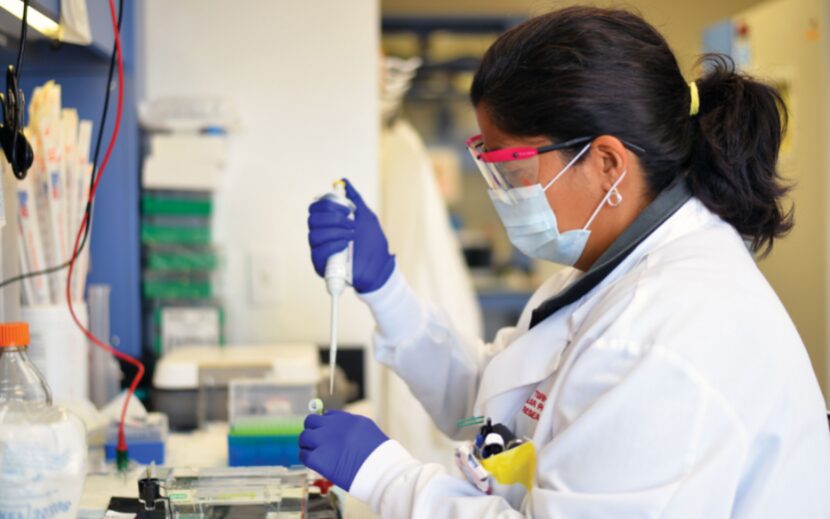 A Scottish Rite researcher works in a lab with a mask, gloves and face shield on.