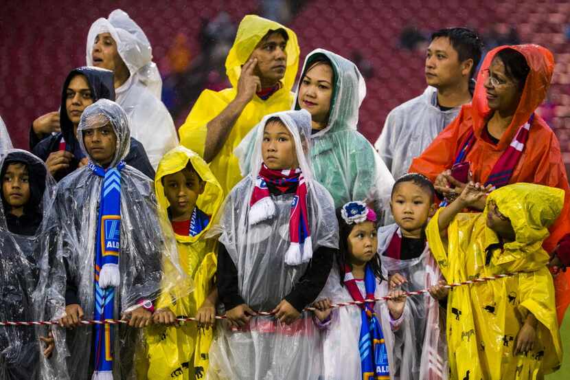 Children and their parents in rain panchos wait for team introductions before FC Dallas took...