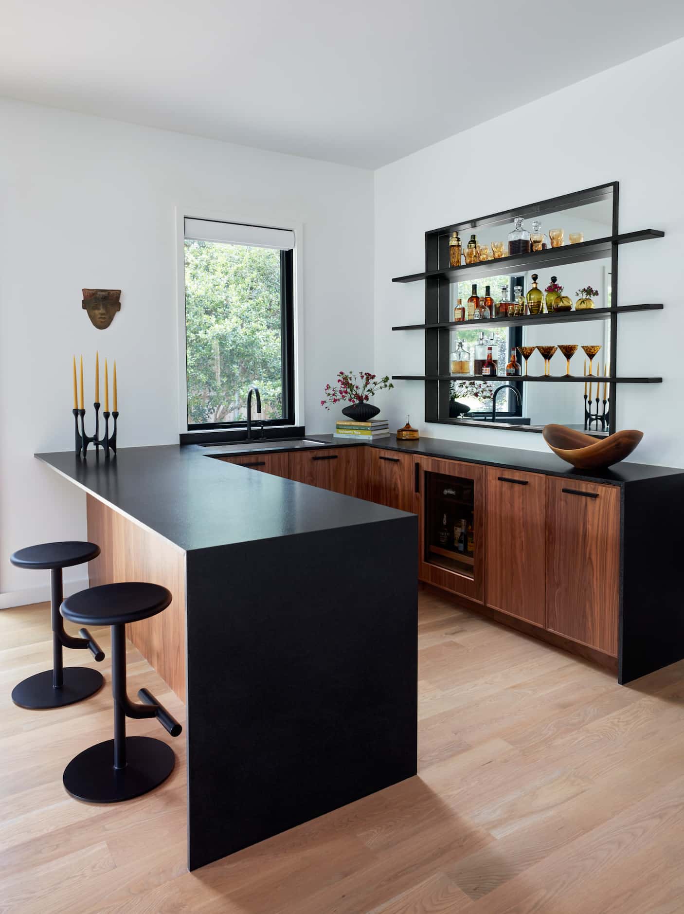 Home wet bar with black waterfall-edge countertop, wood cabinets and open shelving for...