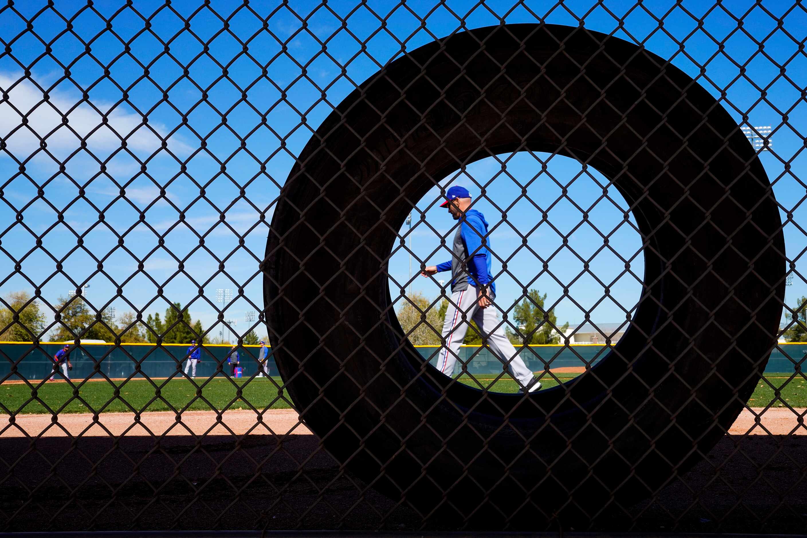 Texas Rangers manager Chris Woodward walks past a tire leaning on the fence of a practice...