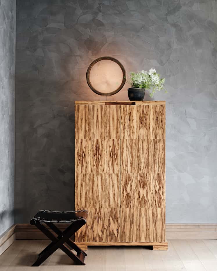 A circular lamp made out of bronze illuminates the space above a decorative cabinet.