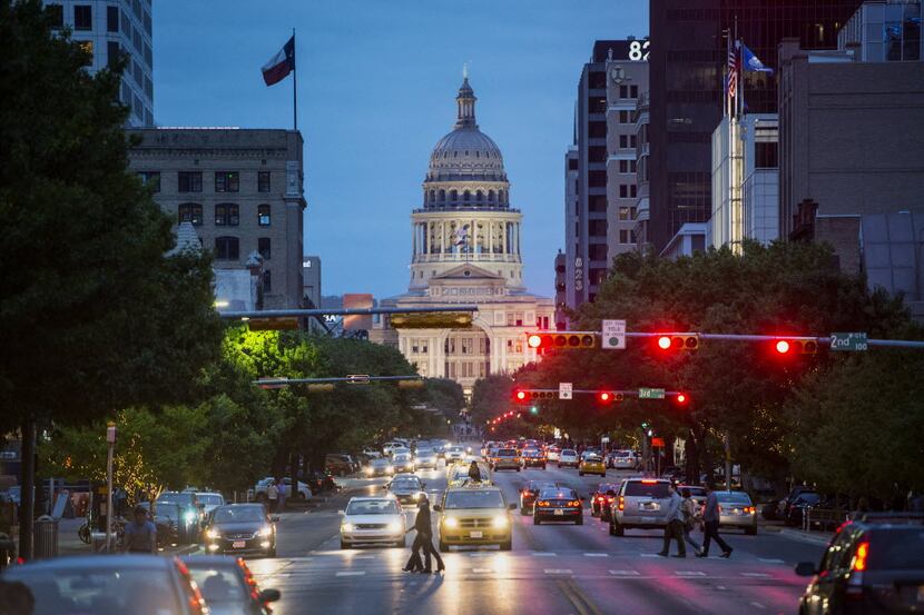 The Texas State Capitol building stands past cars and pedestrians crossing the street at...