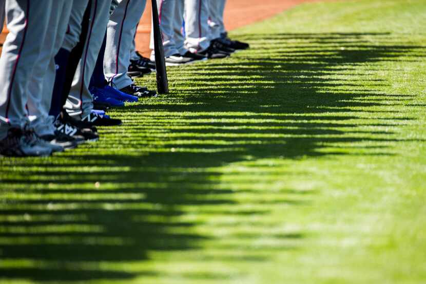 Texas Rangers shadows appear on the grass as they line up for the national anthem before a...