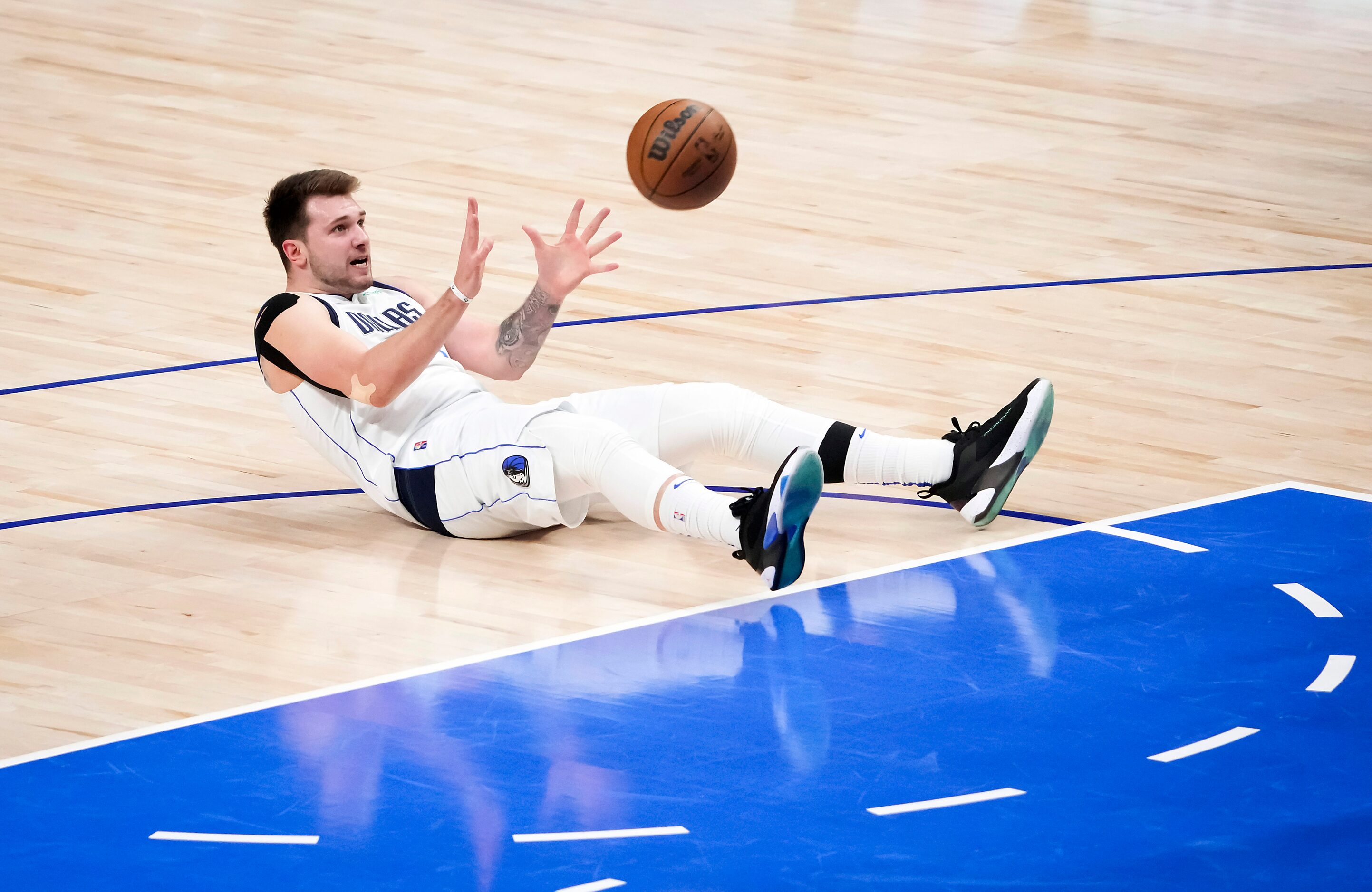 Dallas Mavericks guard Luka Doncic grabs a rebound as he lies on the floor after being...