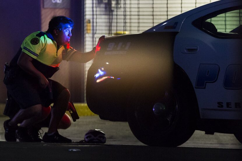 A Dallas police officer crouched behind a squad car as shots rang out Thursday night in...