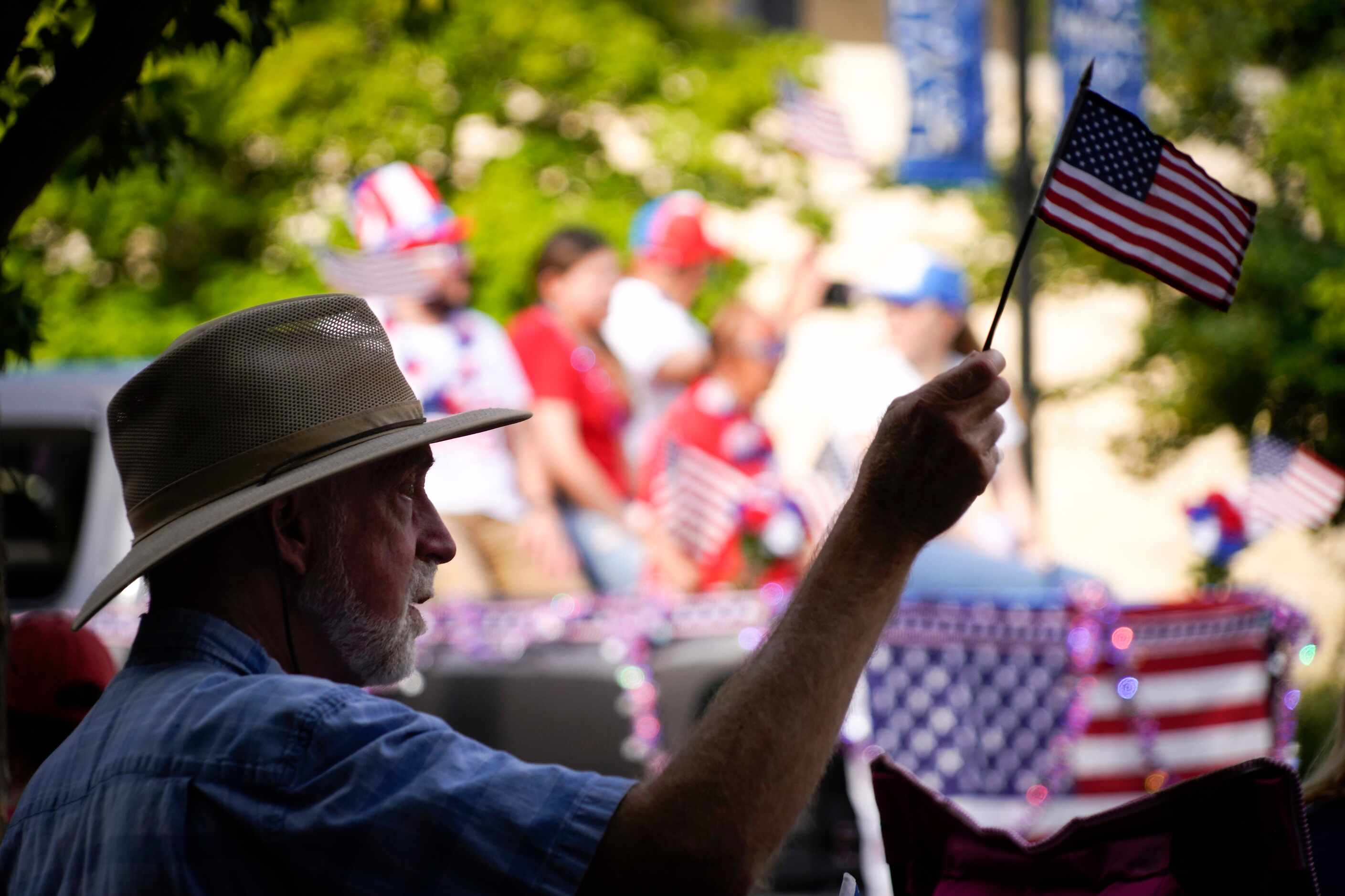 A spectator waves a flag from a shady watching spot during the Arlington Independence Day...