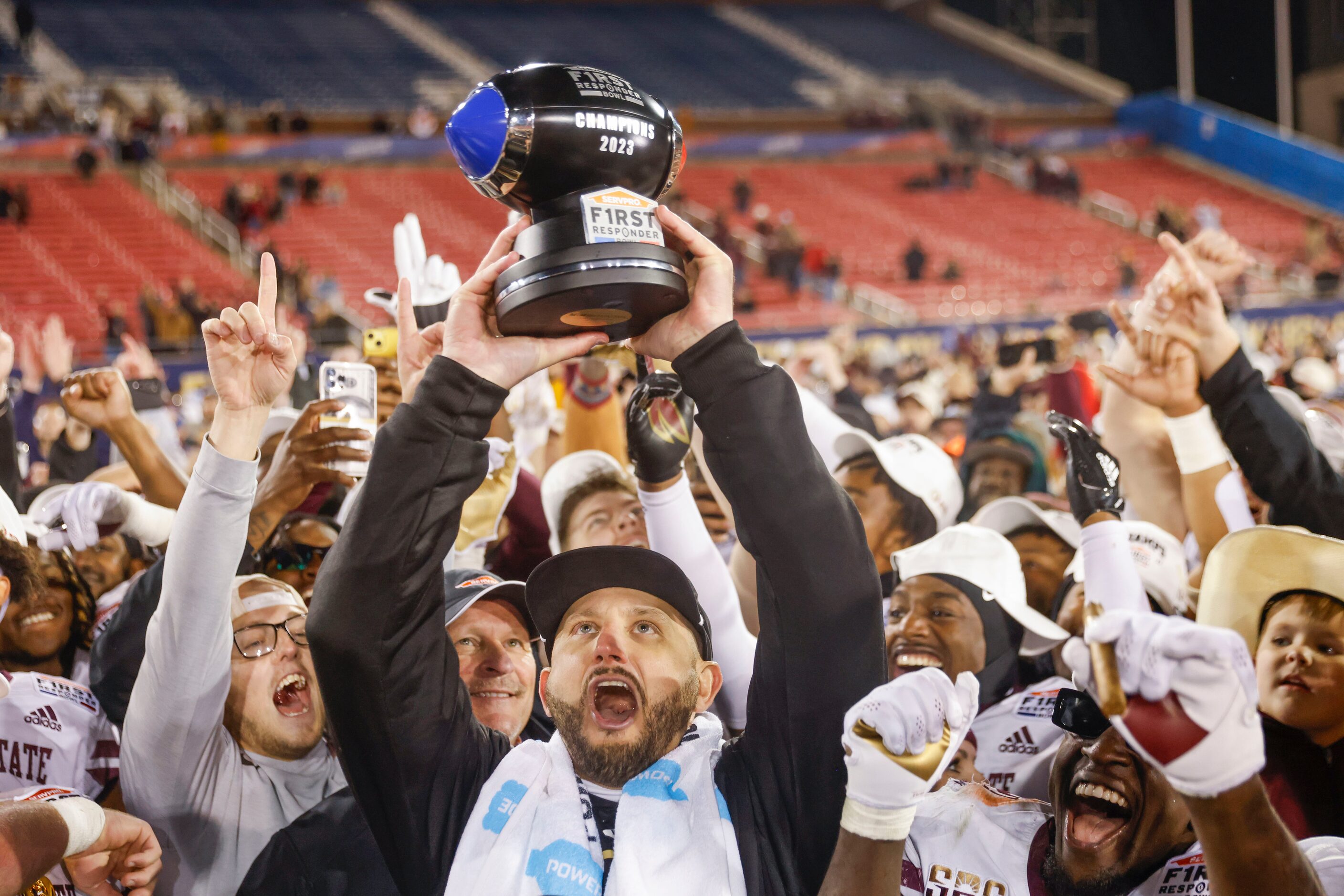 Texas State head coach GJ Kinne lifts the First Responder Bowl trophy as the team celebrates...