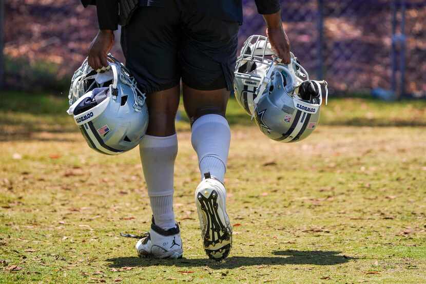 A Dallas Cowboys player carries helmets from the field after a practice at training camp on...
