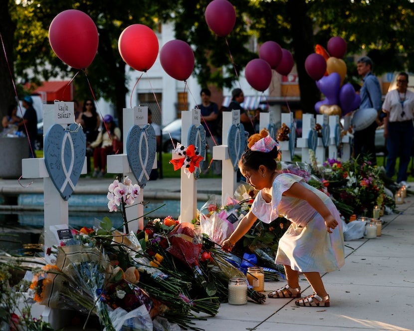 Four-year-old Bella Cazares lays a rose at a cross for fourth grade teacher Eva Mireles...