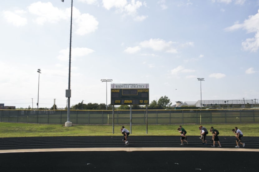 Wrestlers run a lap on the track while carrying a teammate during practice at Birdville High...