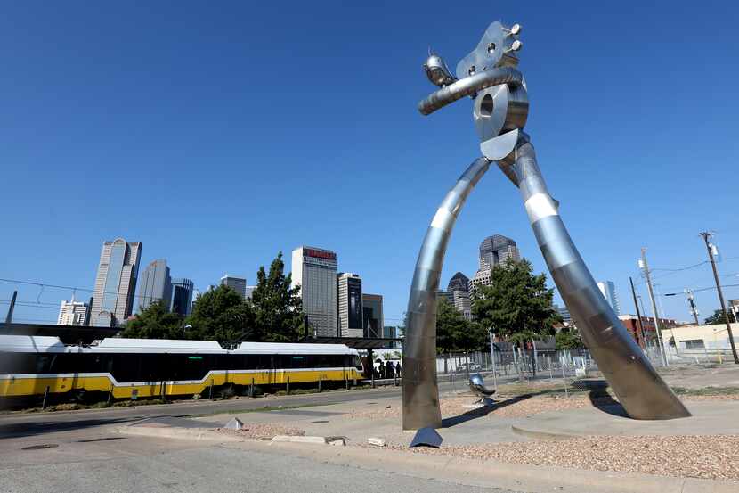 The Traveling Man stands as a DART train goes by at the Deep Ellum station in downtown...
