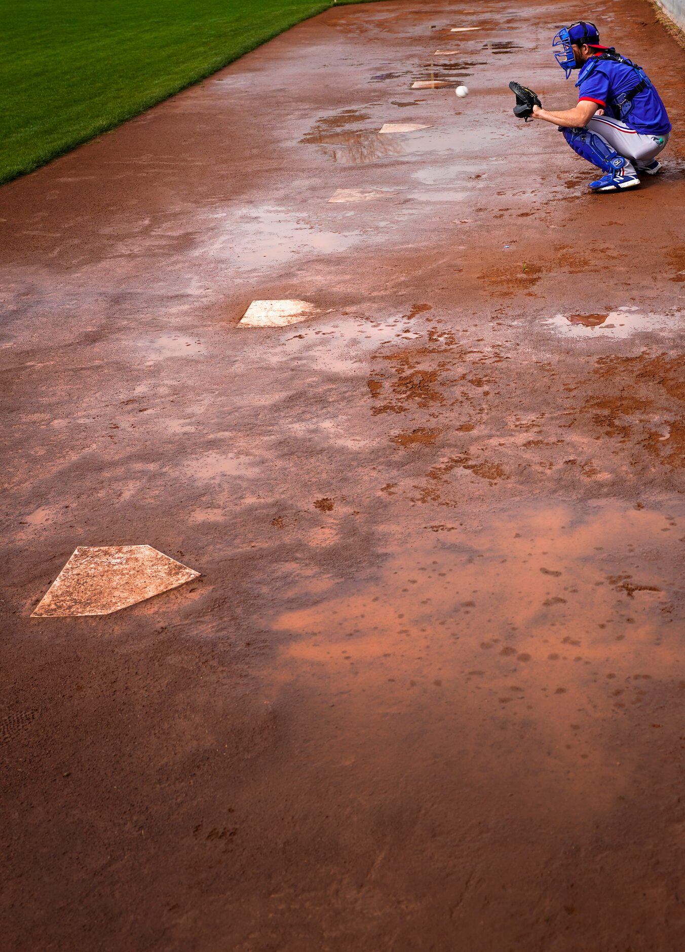 Texas Rangers catcher Jeff Mathis catches for pitcher Kyle Gibson in a muddy bullpen session...