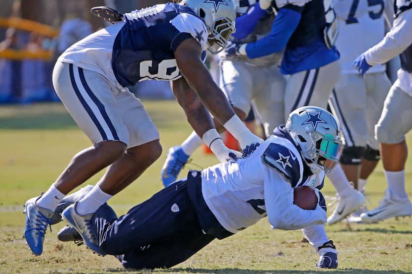 Cowboys defensive end DeMarcus Lawrence (90) pushes running back Ezekiel Elliott (21) to the...