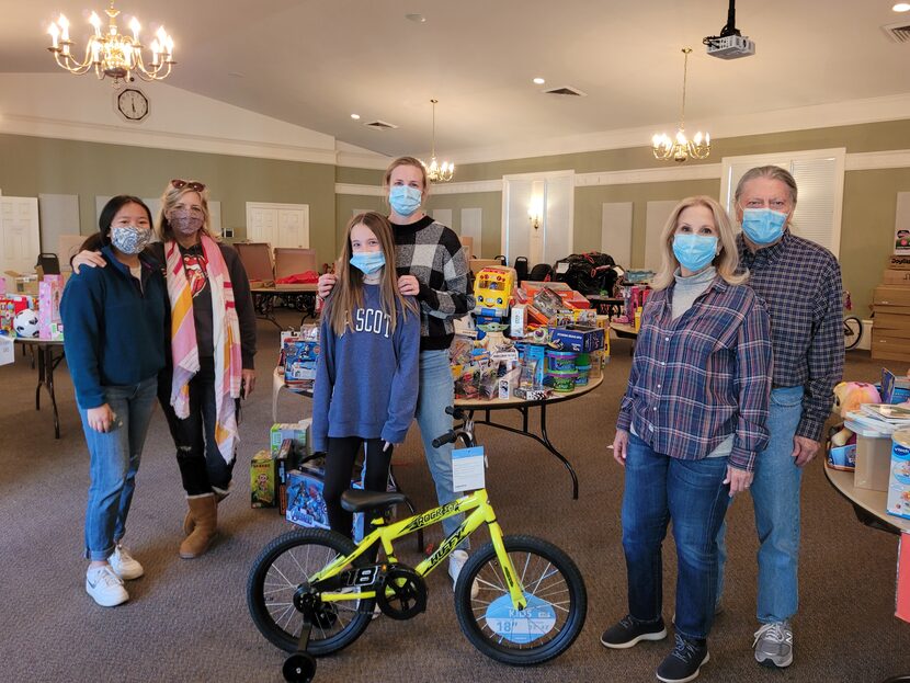 A group of volunteers stand with a bicycle, in a room full of toys donated for the Holidays...