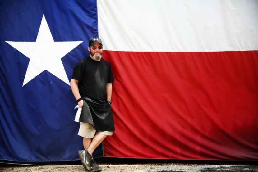 Pitmaster John Mueller poses for a photo in front of his large Texas flag hung from the side...