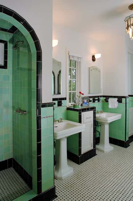 Mint green tile on the walls of a bathroom is bordered by a black tile edge. On the floor, a...