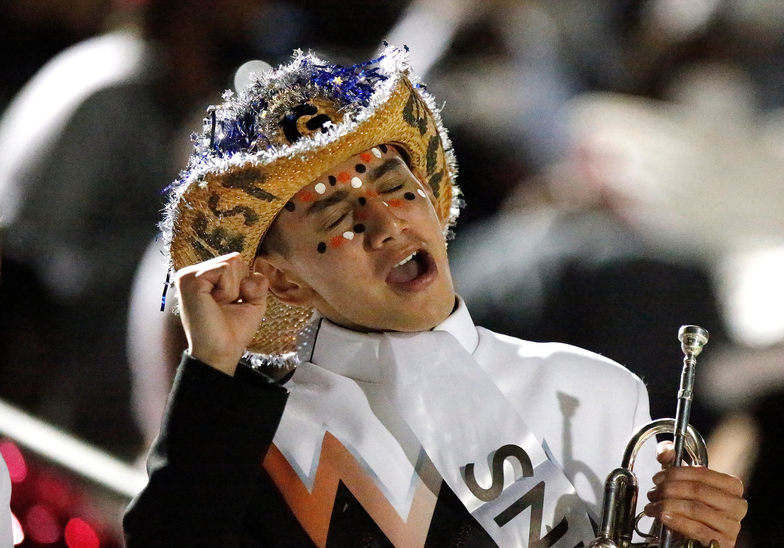West Mesquite marching band member Gio Lumas, 17, holds his trumpet while cheering his team...