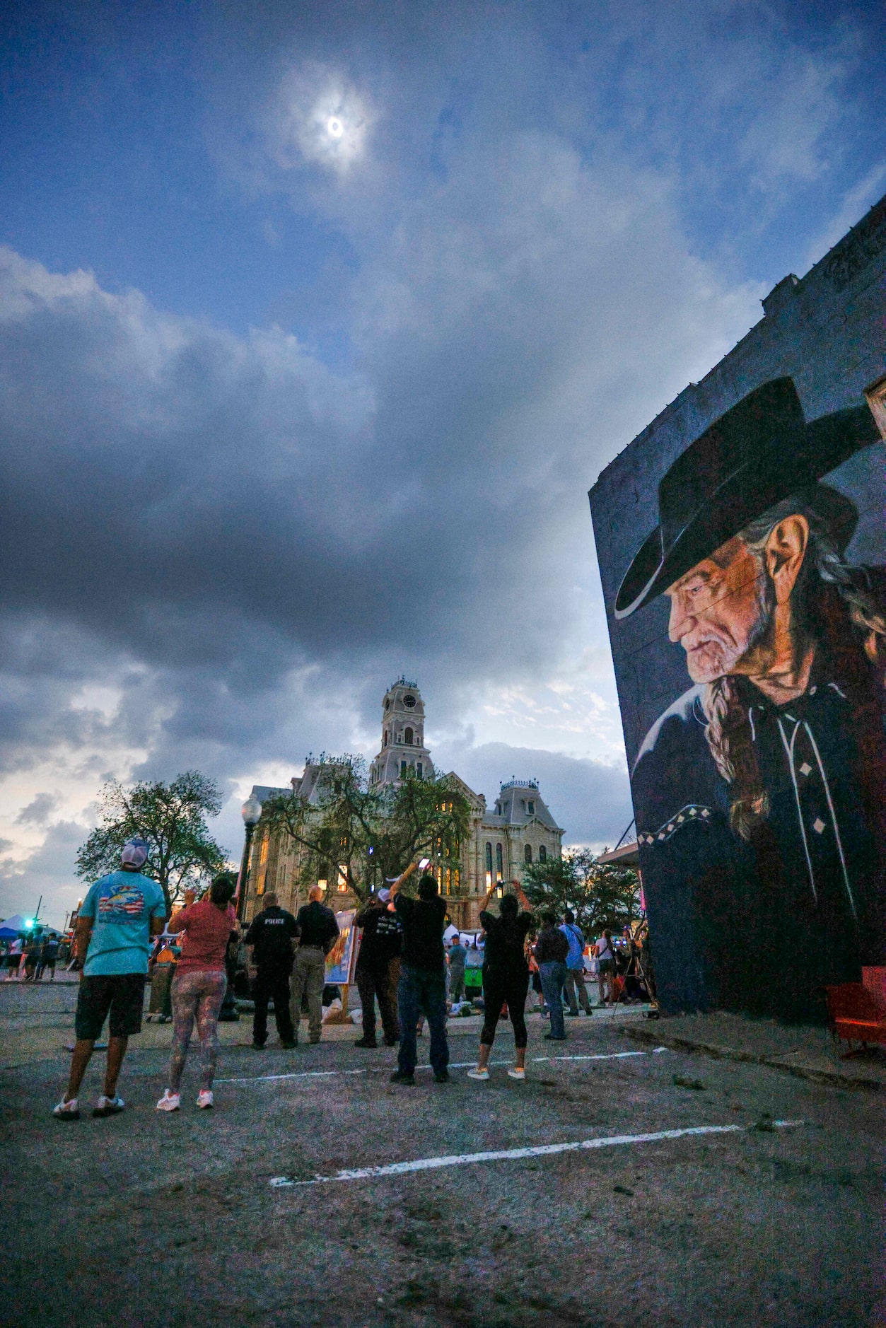 People watch a total solar eclipse over the Hill County Courthouse and a mural of Willie...