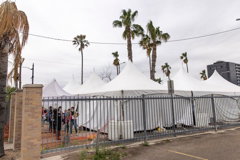 Migrant families with small children wait in line to be tested for COVID-19 at a tent...