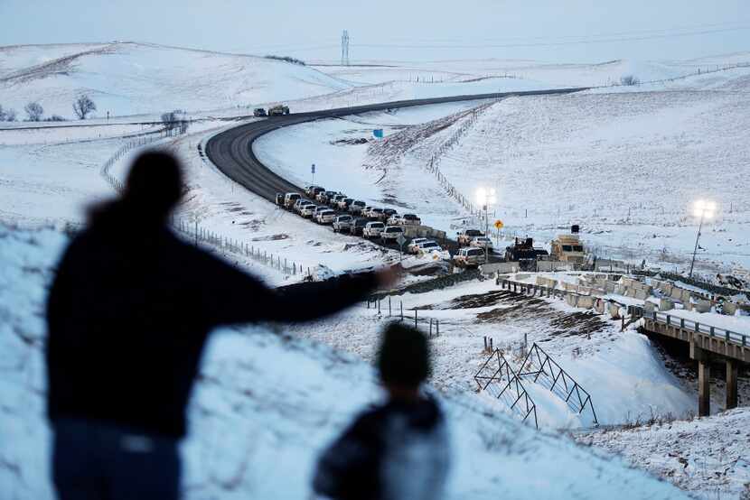 Law enforcement vehicles line a road leading to a blocked bridge next to the Oceti Sakowin...