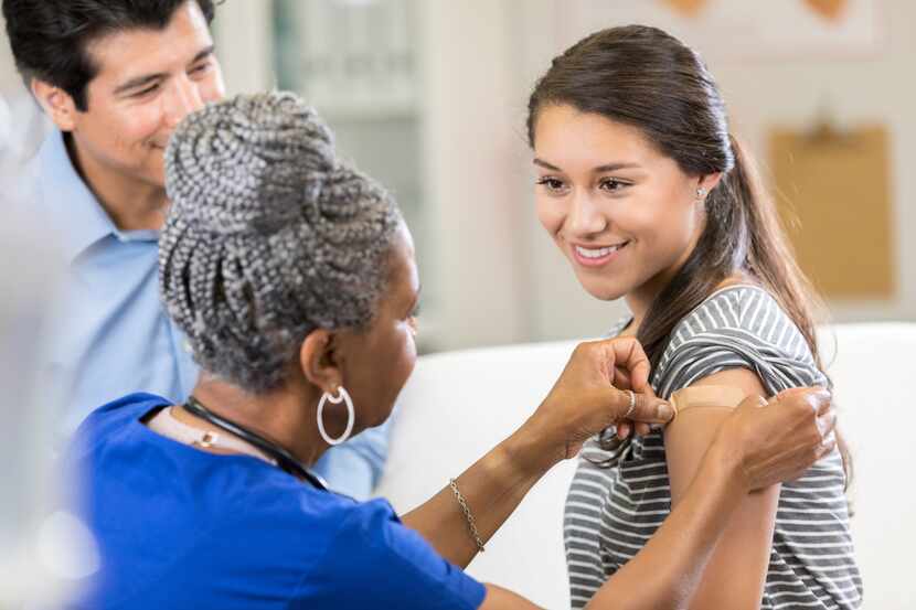 Nurse places a bandage on female teenage patient's arm after administering a flu shot. The...