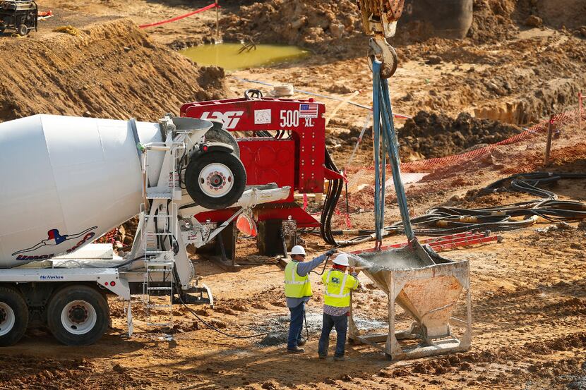 Construction workers wash down a large crane-supported concrete bucket on the Texas Live!...