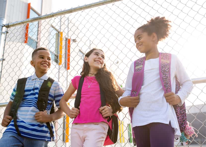 A group of three preteens smiling and leaning against a fence.