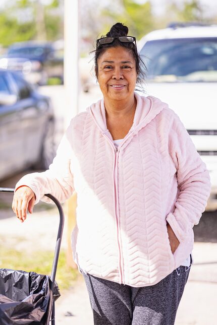 Middle-aged woman in a pink sweater smiles and poses next to a cart.