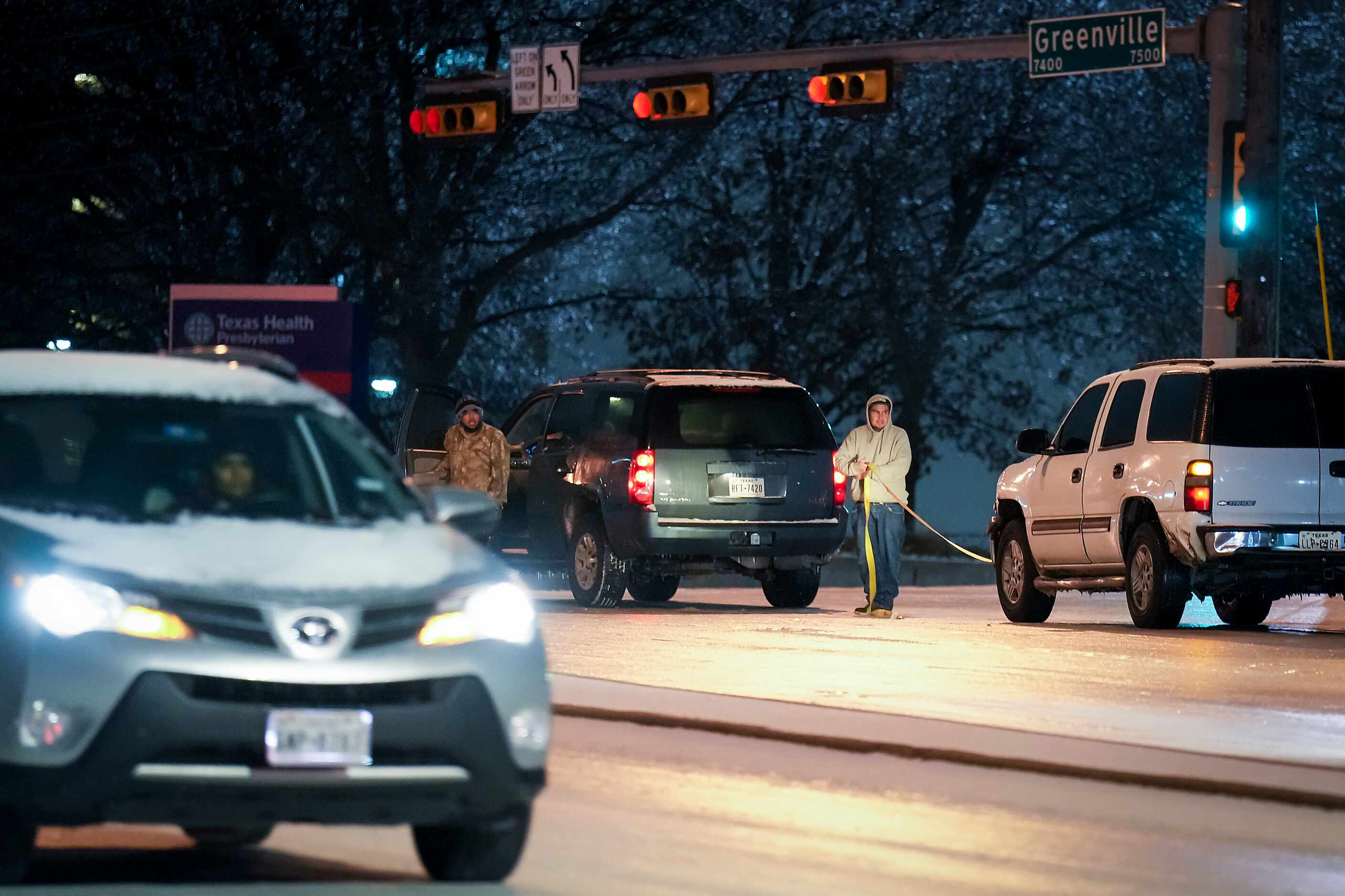 Two men work to pull a stuck vehicle through the icy intersection of Greenville Avenue at...