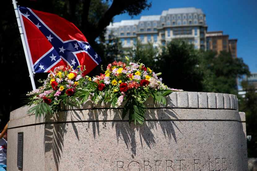 A Confederate flag flies over bouquets of flowers  placed on the Robert E. Lee statue base...
