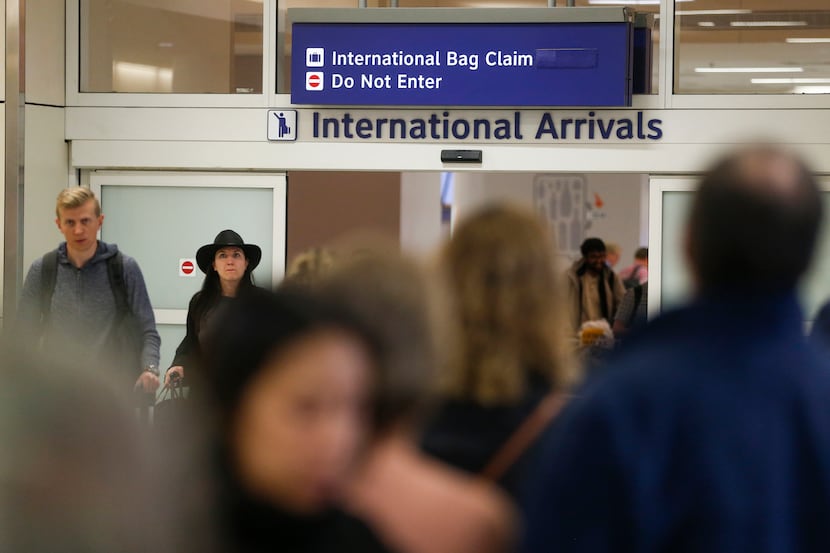 Travelers, some seen wearing protective masks, arrive in the international arrivals area of...