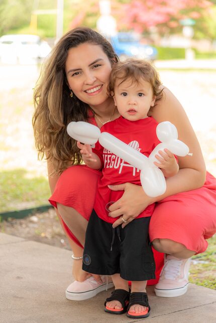 Woman kneels to pose with a toddler holding a balloon animal.