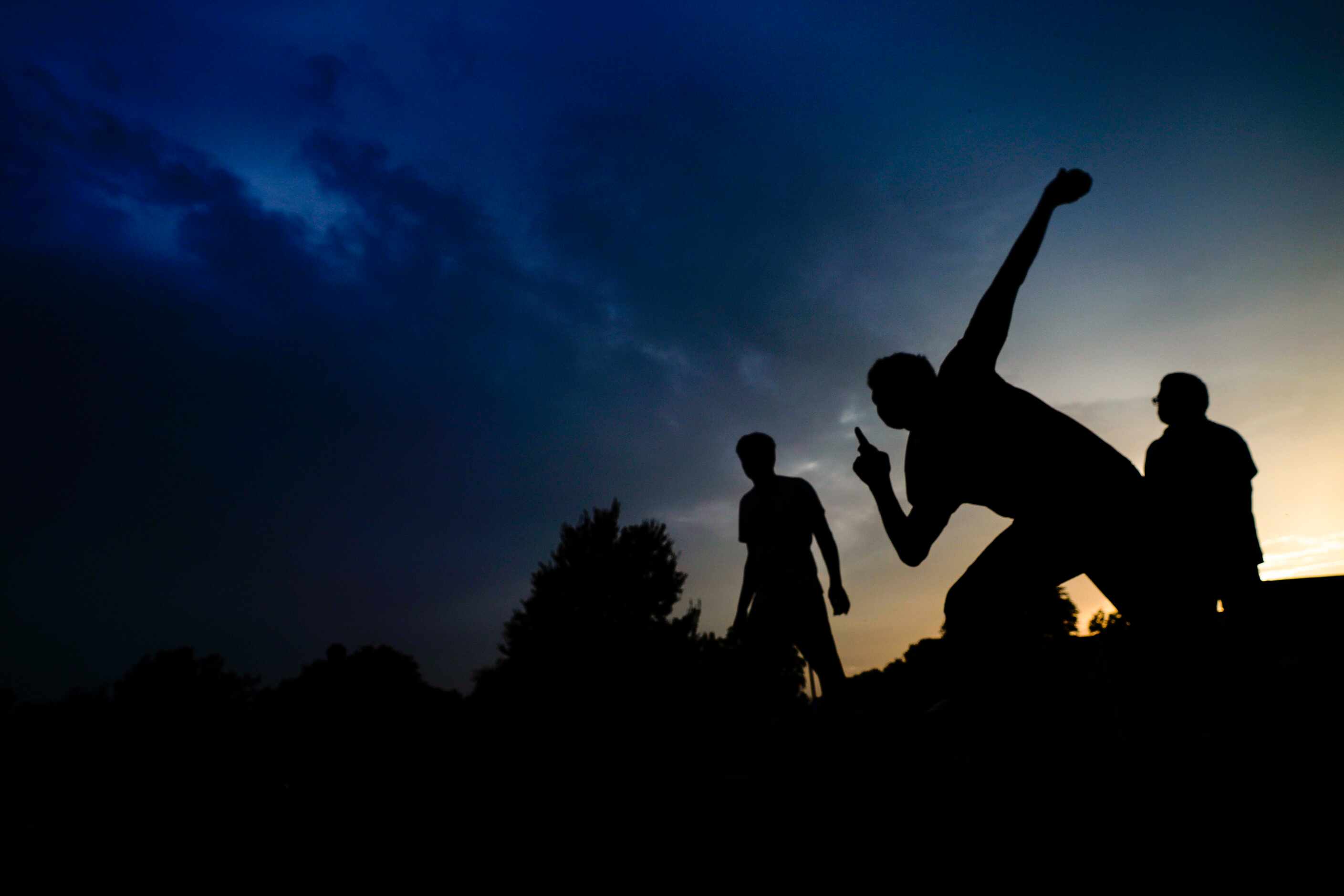 Sinjith Varma is silhouetted against the sunset as he bowls ruing a pickup cricket match on...