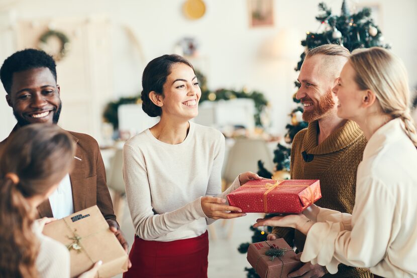 Group of elegant young people exchanging gifts and smiling cheerfully during Christmas party.