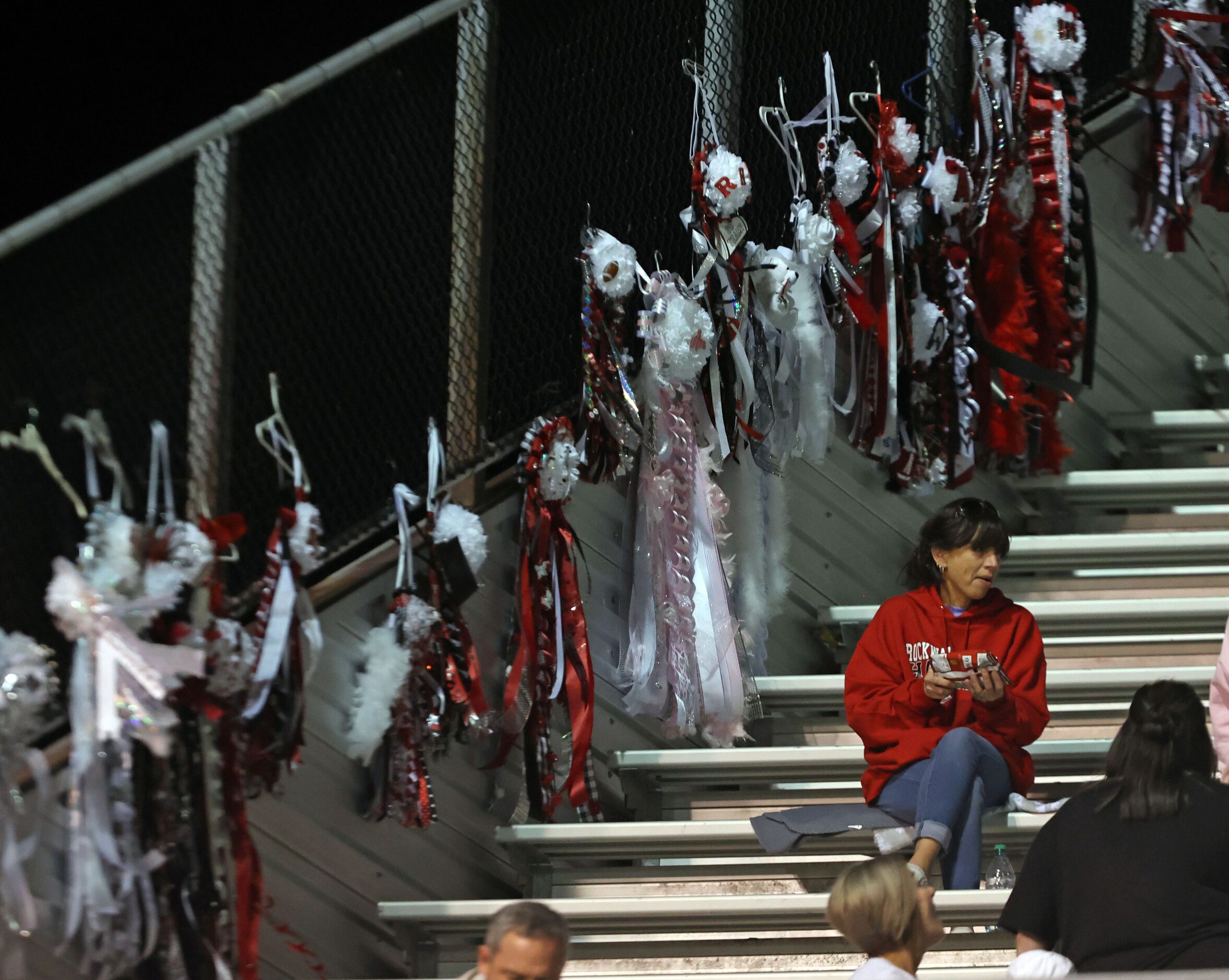 Homecoming mums hang on a stadium fence during the first half of a high school football game...