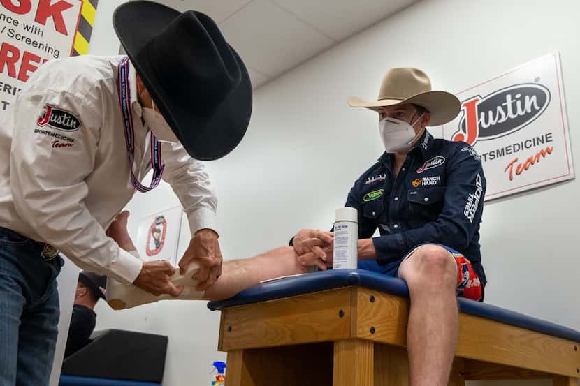 Bullfighter Cody Webster (right) has his ankles taped by sports medicine team program...