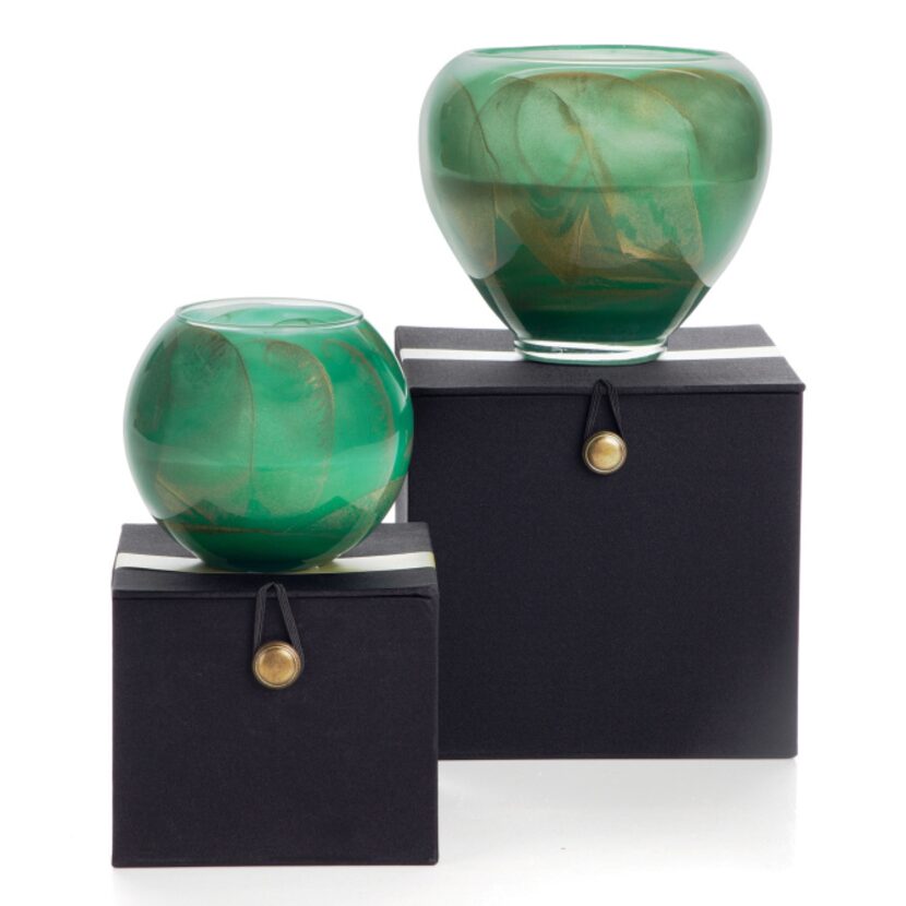 Swirls of gold and green highlight blown-glass, hand-poured Esque candles packaged in a...