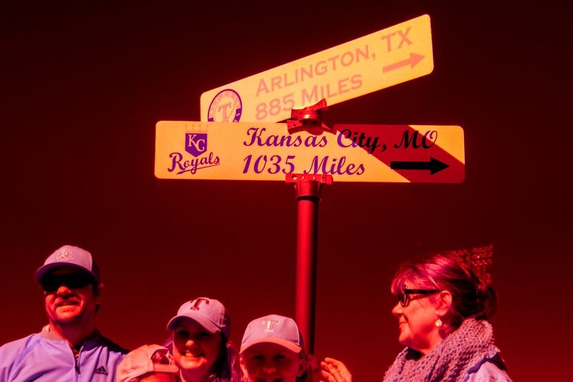 Fans pose for photos near a sign showing the distances to the homes of the Texas Rangers and...