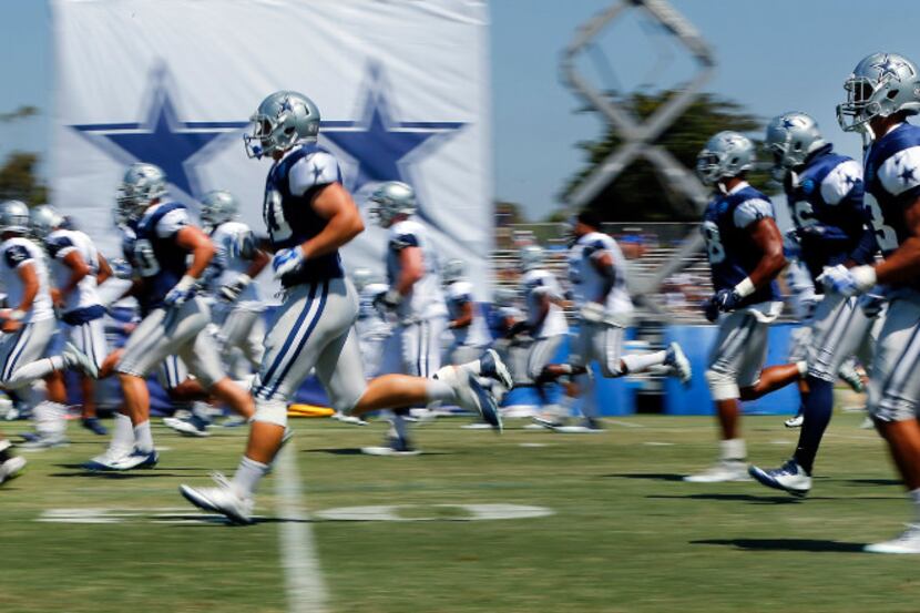 Cowboys players sprint down the field as the warm up for morning practice at training camp...
