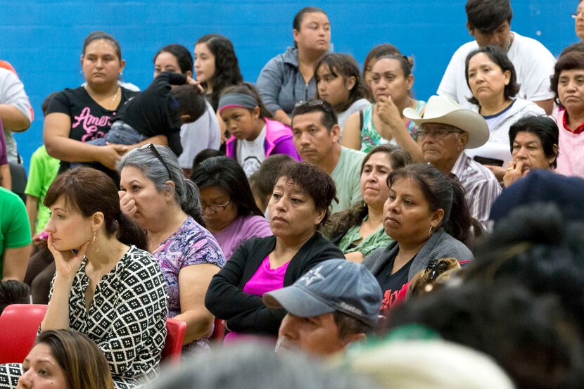 Community members listen to announcements during a community meeting regarding upcoming mass...