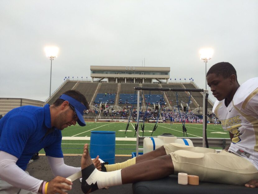 Conrad High School athletic trainer Kirk Kaps tapes the ankle of freshman Carlos Griffin (9)...