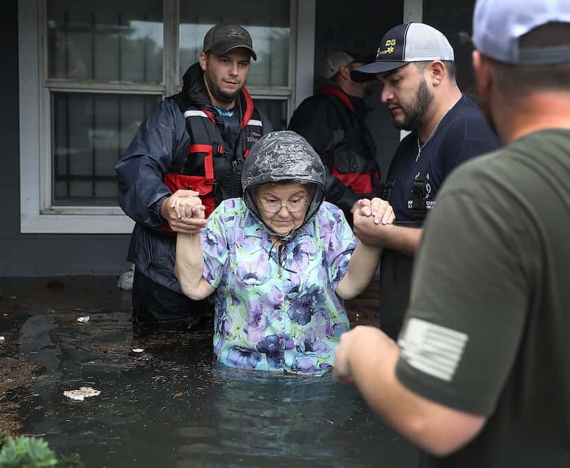 Volunteer rescuer workers help a woman from her home that was inundated with the flooding of...