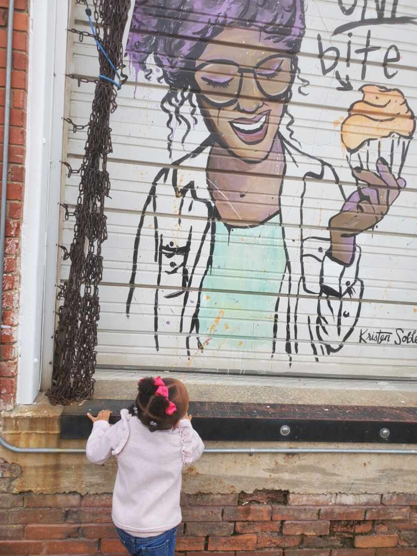 A girl looks up at a mural by Kristen Soble of Tareka Lofton outside of her bakery, Loft 22...