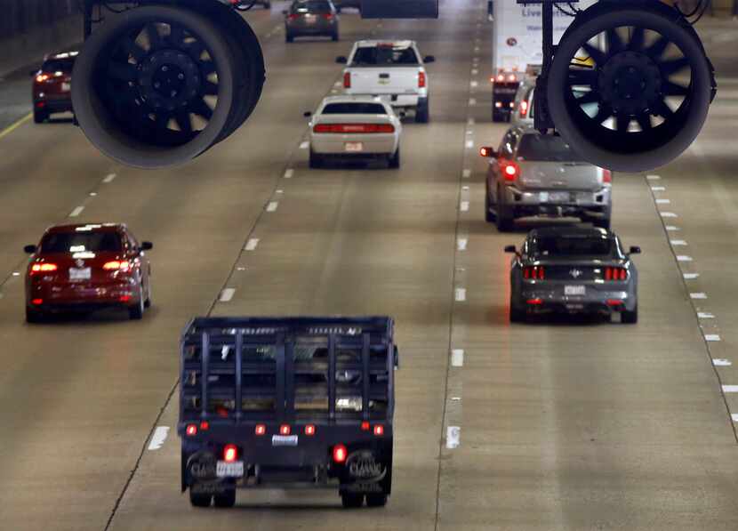 Vehicles on Woodall Rodgers Freeway pass under Klyde Warren Park where large fans are hung...