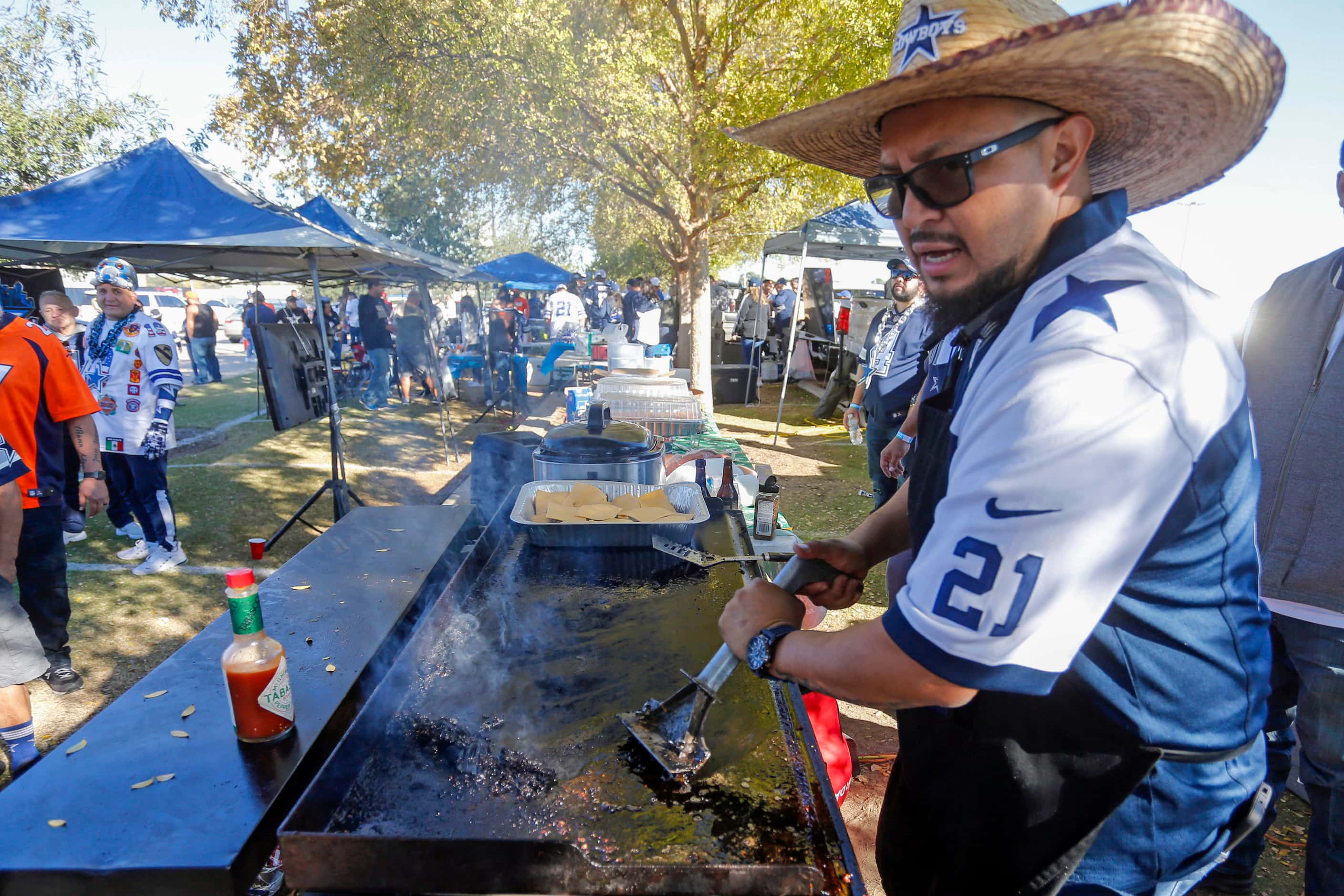Freddy Saracan, of Dallas, cleans up a grill on the parking lot of AT&T Stadium before a NFL...