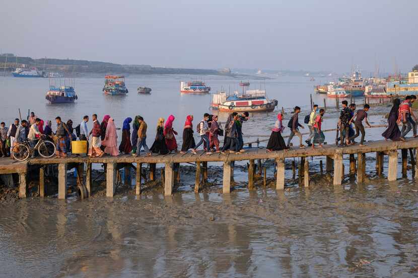 Decenas de personas caminan hacia sus trabajos en Mongla (Bangladesh), cruzando a pie el río...