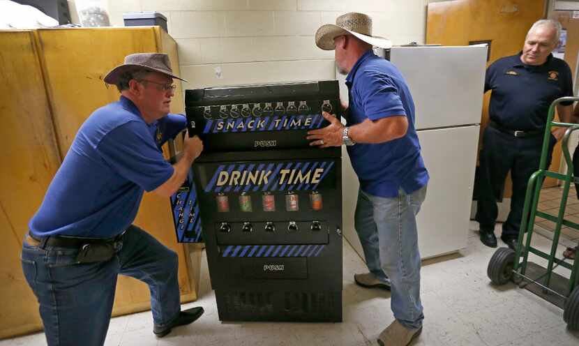 Patrick Travers (left) and Kelly Walker (center) install a drink machine stocked with soft...