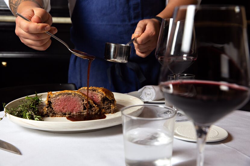 Chef Ji Kang pours bordelaise sauce onto a plate of Dakota’s beef Wellington. 